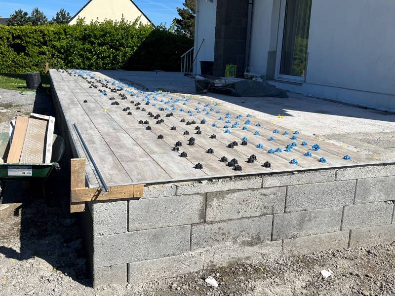 Pose des rangées de carrelage en grès céramique pour la construction d'une terrasse par Les Paysagistes du Trégor à Pleumeur-Bodou