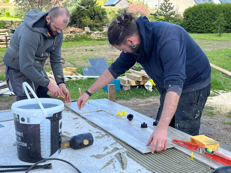 Pose du premier carreau de carrelage pour la construction d'une terrasse en grès céramique par les Paysagistes du Trégor à Pleumeur-Bodou